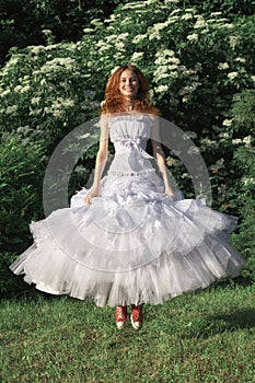 Cheerful beautiful bride jumping outdoors in white wedding dress and red sneakers. Funny concept