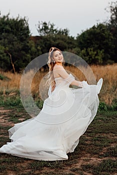 a cheerful, beautiful bride, laughing and looking around, runs across the field in a wedding dress