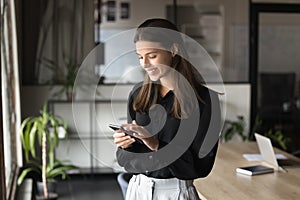 Cheerful beautiful businesswoman typing on smartphone, using professional service