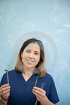 Cheerful and beautiful dentist holding instrumentation and smiling in dental clinic