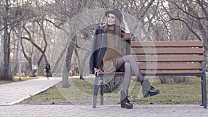 Cheerful beautiful girl in hat sitting on bench in sunny autumn park. Action. Beautiful young woman in hat sitting on