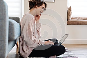 Cheerful beautiful girl working with laptop while sitting on floor