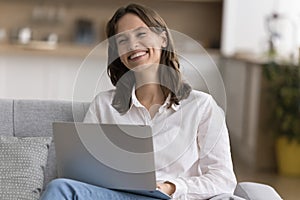 Cheerful beautiful laptop user woman sitting on home couch photo