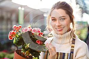 Cheerful beautiful woman florist holding flowering begonia