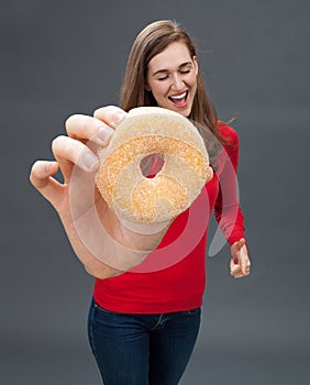 Cheerful beautiful woman holding a big appetizing donut as temptation