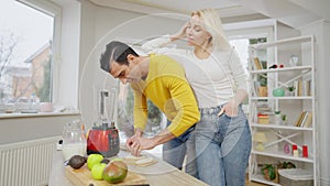 Cheerful beautiful woman leaning on man cutting banana for healthful dieting smoothie. Positive Caucasian wife and