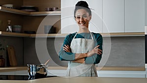 Cheerful beautiful woman wears apron standing in modern kitchen with crossed hands smiling happy housewife maid chef