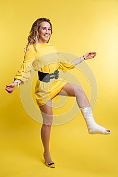Cheerful beautiful woman in yellow dress having fun with plaster on her leg.