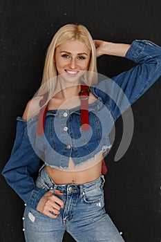 Cheerful beautiful young attractive happy woman with a smile in fashionable denim clothes with blue jeans near the black wall.