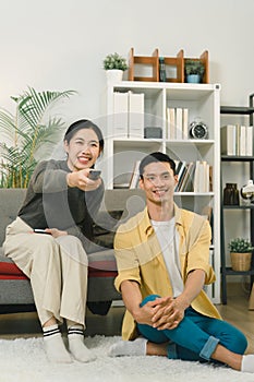 A cheerful, beautiful young couple can be seen relaxing on the couch in their cozy home, with their eyes glued to the TV