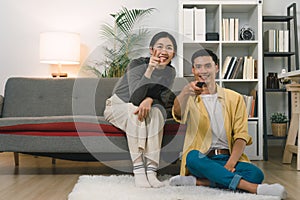 A cheerful, beautiful young couple can be seen relaxing on the couch in their cozy home, with their eyes glued to the TV