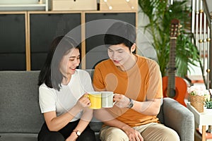 Cheerful beautiful young couple drinking coffee together on sofa in the morning.