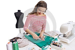 Cheerful beautiful young girl, seamstress, dressmaker working with fabric, scissors and sewing machine isolated on white