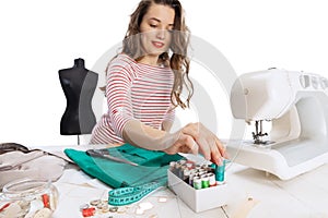 Cheerful beautiful young girl, seamstress, dressmaker working with fabric, scissors and sewing machine isolated on white