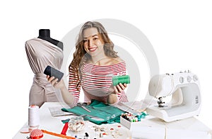 Cheerful beautiful young girl, seamstress, dressmaker working with fabric, scissors and sewing machine isolated on white