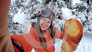 Cheerful beautiful young girl snowboarder makes selfie on an action camera or smartphone, smiling. A woman is standing