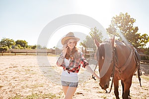 Cheerful beautiful young woman cowgirl with her horse on ranch