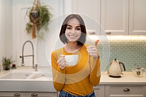 Cheerful beautiful young woman enjoying herbal tea at home