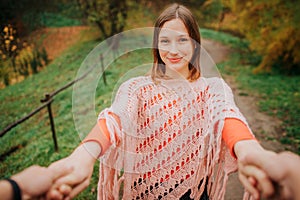 Cheerful and beautiful young woman hold man`s hands and look on camera. She stands on meadow. Young woman looks