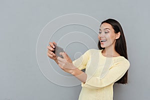 Cheerful beautiful young woman playing video games on mobile phone