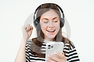 Cheerful, beautiful young woman using smartphone app, celebrating, looking happy while playing with mobile phone