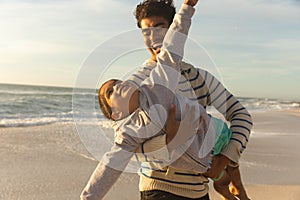 Cheerful biracial man carrying daughter pretending to fly at beach against sky on sunny day