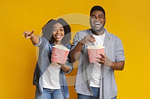 Cheerful black couple eating popcorn from buckets and laughing at camera