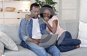 Cheerful black couple using laptop together at home