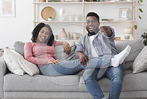 Cheerful black couple watching comedy movie on tv and laughing