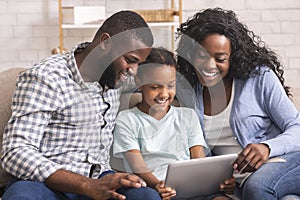 Cheerful black family using digital tablet together at home
