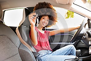 Cheerful black female showing key in automobile