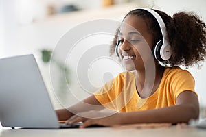 Cheerful black girl studying online, using laptop and headset