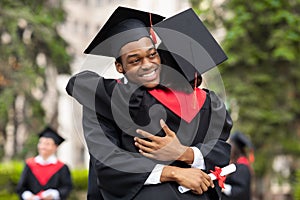 Cheerful black guy hugging his girlfriend while graduation ceremony