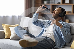 Cheerful Black Guy Listening Music In Wireless Headphones And Singing At Home