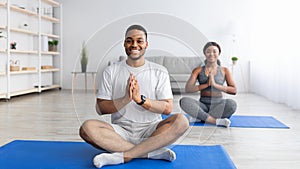 Cheerful black guy meditating or doing breathing exercises, practicing yoga with his girlfriend at home, banner design