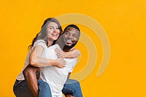 Cheerful black guy piggibacking his girlfriend, interracial couple having fun together photo