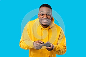 Cheerful Black Guy Playing Videogame Holding Game Controller, Blue Background