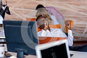 Cheerful black guy is watching at his laptop screen, at his work place, with arms behind the head.