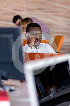 Cheerful black guy is watching at his laptop screen, at his work place, with arms behind the head.