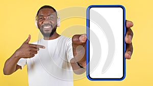 Cheerful Black Guy Wearing Headphones Showing Huge Smartphone, Yellow Background