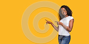 Cheerful black lady pointing at copy space on yellow photo