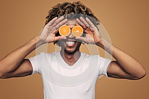 Cheerful black man covering eyes with oranges