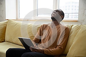 Cheerful black man laughing watching videos online on digital tablet