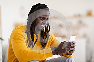 Cheerful Black Man Messaging On Mobile Phone While Relaxing At Home