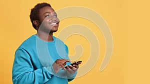 Cheerful black man using modern smartphone, portrait in orange background in studio, chatting in app