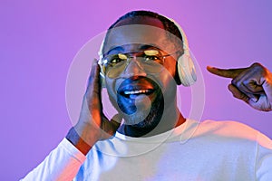 Cheerful black man using wireless headphones, pointing at gadget