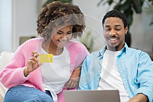 Cheerful black man, woman using laptop, bank card at home