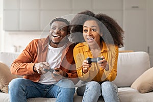 Cheerful black millennial couple playing video games at home