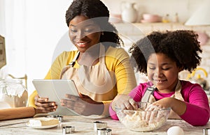 Cheerful Black Mom And Daughter Using Digital Tablet In Kitchen, Checking Recipe