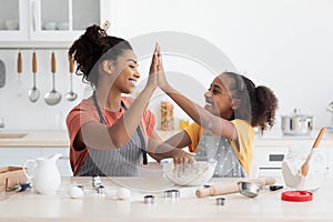 Cheerful black mother and daughter giving high five while cooking